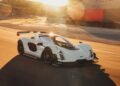 A white Czinger 21C sports car with a large rear wing drives on the Laguna Seca racetrack at sunset, motion blur emphasizing its speed.