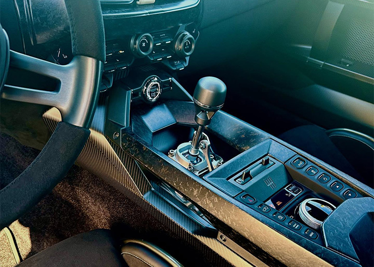 Close-up view of a car’s center console featuring a manual gear shift, control buttons, air conditioning dials, and carbon fiber trim.