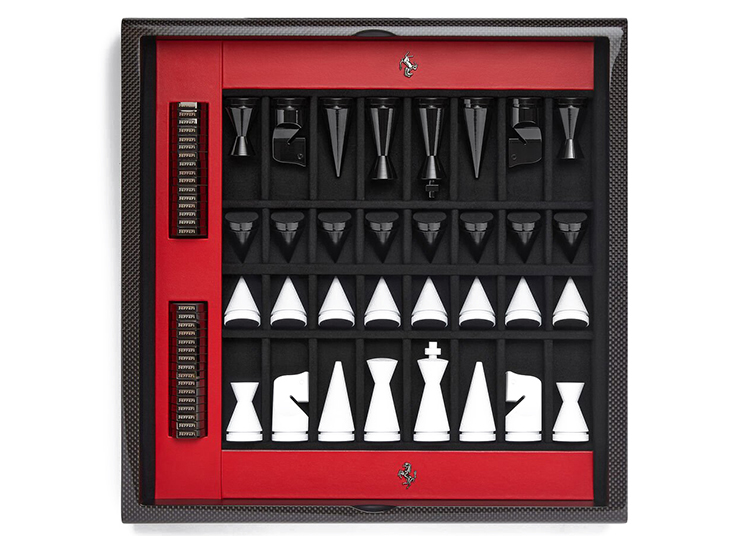 A modern chess set featured in the duPont REGISTRY 2026 Holiday Gift Guide, with black and white geometric pieces on a red and black board, metallic logo details, and score markers on the left side.
