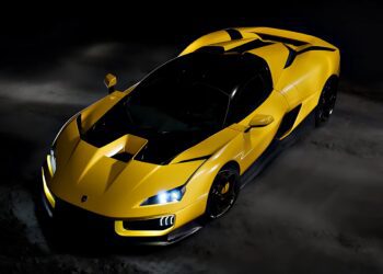 A yellow sports car with black accents is parked on a dark surface, illuminated from above, highlighting its sleek and angular design—echoing the spirit of 20 Cars That Focused on Analog Engagement in 2025.