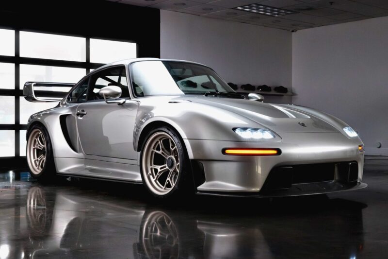 A silver sports car with aerodynamic bodywork and a large rear wing is parked indoors on a polished floor under ceiling lights—one of the 20 Cars That Focused on Analog Engagement in 2025.