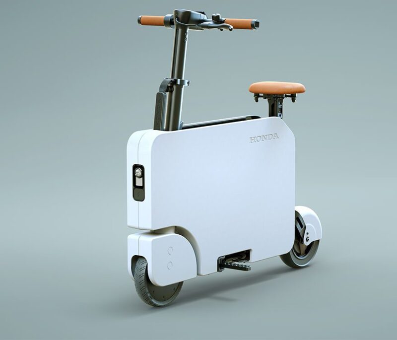 A compact, modern white Honda electric scooter with a rectangular body, brown seat, and two small wheels is featured against a plain background—perfect for the 2026 duPont REGISTRY Holiday Gift Guide.