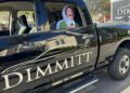 A cardboard cutout of a woman with an excited expression is placed in the backseat of a black pickup truck with "DIMMITT" branding on the door, ready to join the Dimmitt Automotive Group Exotic Car Rally.