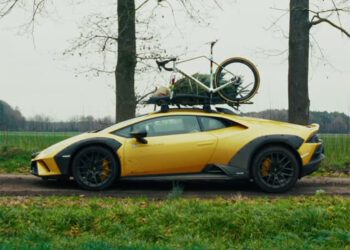 An Off-Road Lamborghini, with a bicycle and a small Christmas tree secured to its roof, is parked on a rural dirt road next to trees and grass—ready for a World Champion Cyclist’s adventurous holiday getaway.