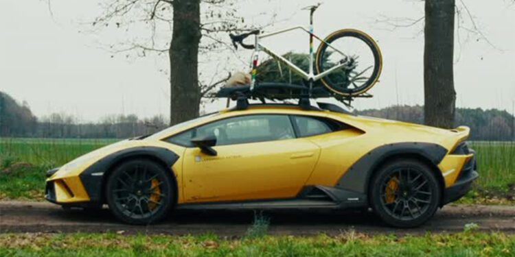An Off-Road Lamborghini, with a bicycle and a small Christmas tree secured to its roof, is parked on a rural dirt road next to trees and grass—ready for a World Champion Cyclist’s adventurous holiday getaway.