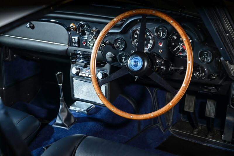 Classic car interior featuring a wooden steering wheel, manual gear stick, analog gauges, and black leather seats—evoking the timeless elegance of a rare car like the iconic Aston Martin DB5.