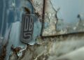 Close-up of a weathered car badge reading "DB5" on a rusted, peeling blue vehicle surface—a glimpse at a rare DB5 once crafted by Aston Martin Works.