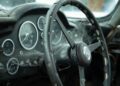 Close-up of a dusty, old Aston Martin DB5 steering wheel and dashboard with visible cobwebs and worn surfaces—capturing the vintage charm of this rare DB5.