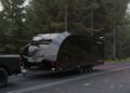 A black Race Transporter 7 enclosed car hauler labeled "RT17" is being towed by a dark pickup truck on a forested road, showcasing the quality of Brian James Trailers.