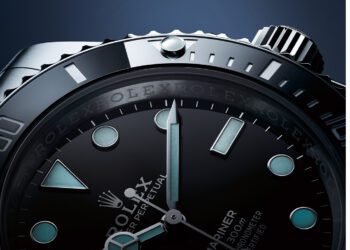 Close-up of a Rolex Submariner watch face, a true collector classic, with luminescent hour markers, rotating bezel, and minute and hour hands set against a dark blue background.