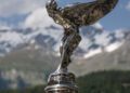 Close-up of the Spirit of Ecstasy hood ornament on a Rolls-Royce, set against snowy mountains and blue sky, as Rolls-Royce marks 150 years of Charles Sykes—the artist behind this iconic masterpiece.