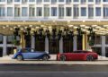 A vintage blue car and a modern red car are parked side by side in front of The Chancery Rosewood hotel building.