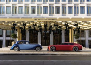 A vintage blue car and a modern red car are parked side by side in front of The Chancery Rosewood hotel building.