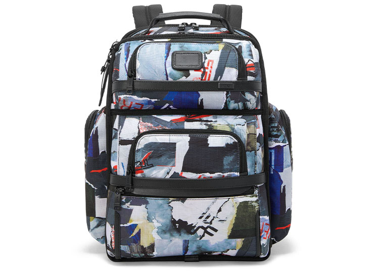 A multicolored, abstract-patterned backpack with multiple zippered compartments and adjustable shoulder straps, featured in the 2026 duPont REGISTRY Holiday Gift Guide and shown against a white background.