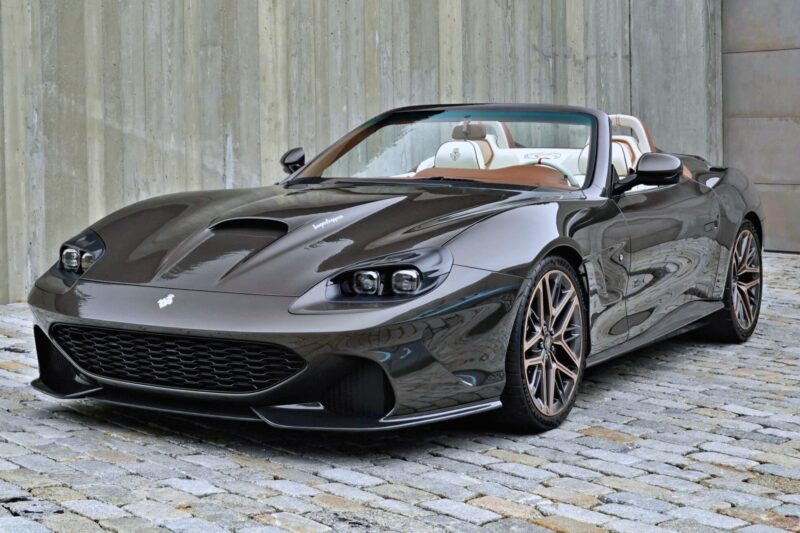 A sleek, dark-gray convertible sports car with tan leather interior is parked on a cobblestone surface in front of a concrete wall—one of the 20 Cars That Focused on Analog Engagement in 2025.