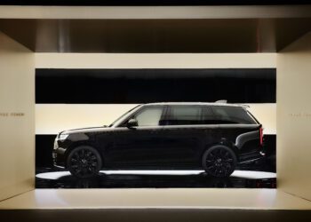 A black Range Rover SUV is displayed in a minimalist, light-colored showroom with bright horizontal light panels.