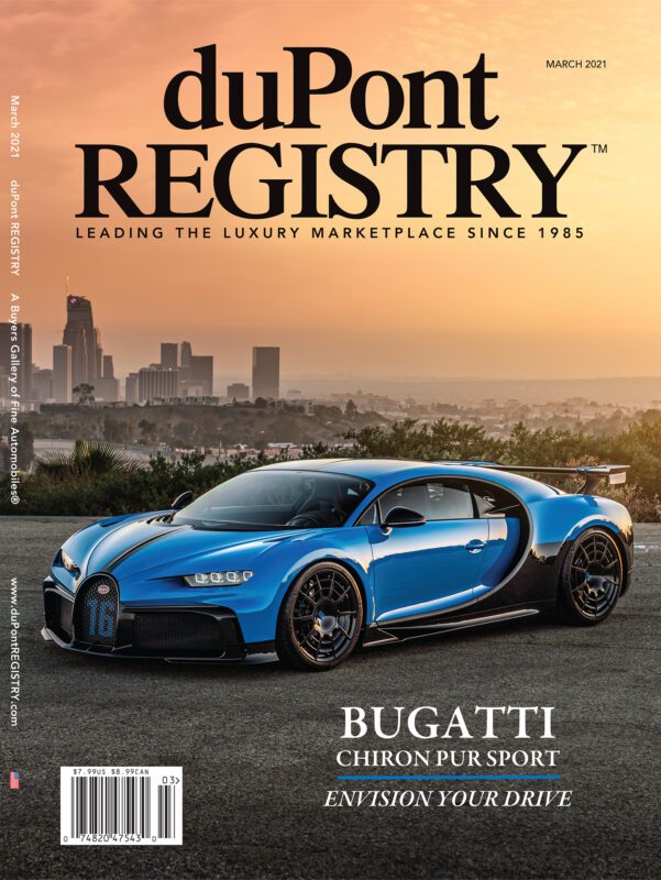 A blue Bugatti Chiron Pur Sport, one of the iconic Cover Cars for duPont REGISTRY's 40th Anniversary, is parked on a road with a city skyline and sunset in the background. The cover text reads "duPont Registry March 2021.
