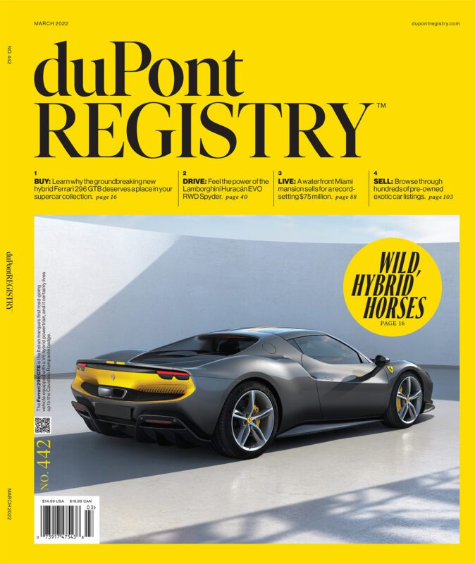 A silver Ferrari 296 GTB sports car is parked in front of a bright yellow wall, gracing the March 2022 duPont REGISTRY Cover Cars issue during their 40th Anniversary celebration.