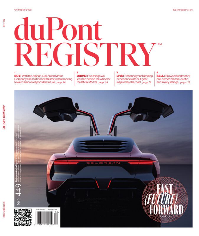 A DeLorean sports car with its gull-wing doors open is shown from the rear under dramatic lighting, featured as one of the Cover Cars celebrating the 40th Anniversary on the duPont REGISTRY magazine, October 2022 issue.