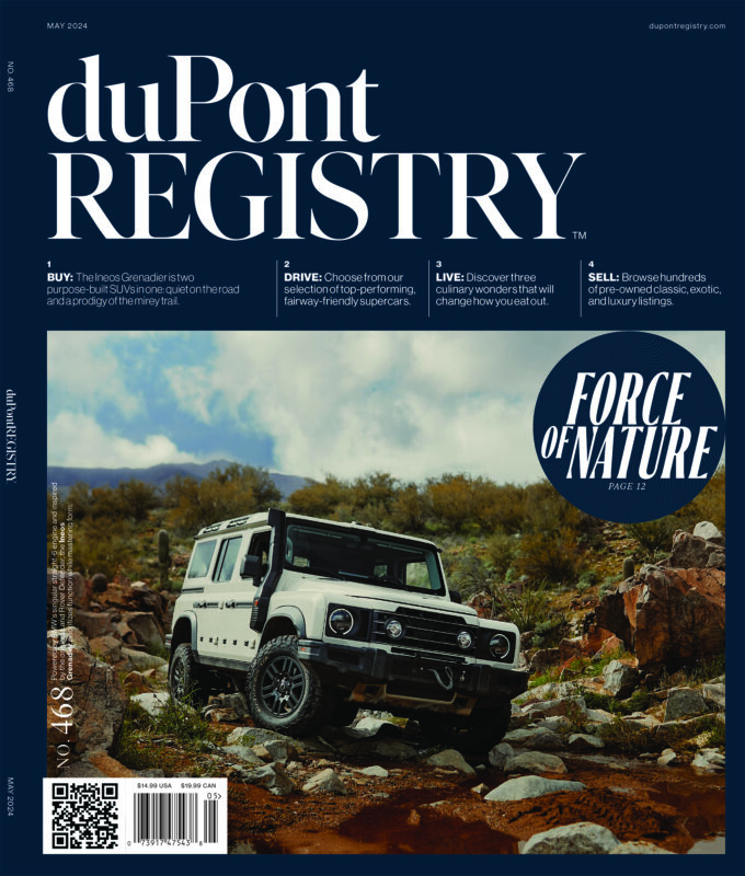 A white Land Rover Defender is parked on a rocky dirt path in front of grassy hills under a cloudy sky; the May 2024 duPont REGISTRY magazine celebrates 40th Anniversary Cover Cars.