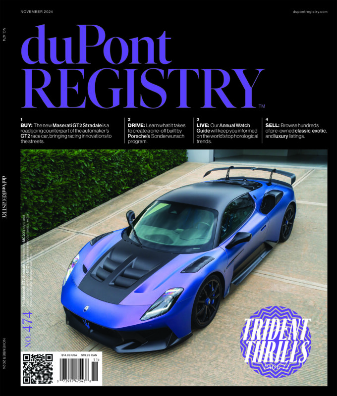 A blue Maserati MC20 sports car is parked on a beige concrete driveway, highlighted as one of the Cover Cars on the November 2024 duPont REGISTRY magazine celebrating its 40th Anniversary.