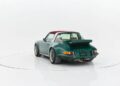 A green classic Porsche sports car with a red convertible top is shown from the rear in a white studio setting.
