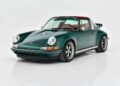 A classic dark green Porsche sports car with a red roof and tan interior is parked on a white reflective surface, viewed from the front left angle.