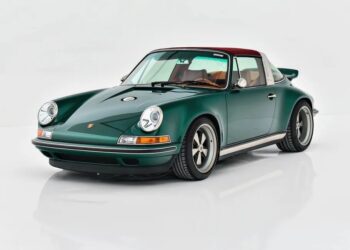 A classic dark green Porsche sports car with a red roof and tan interior is parked on a white reflective surface, viewed from the front left angle.