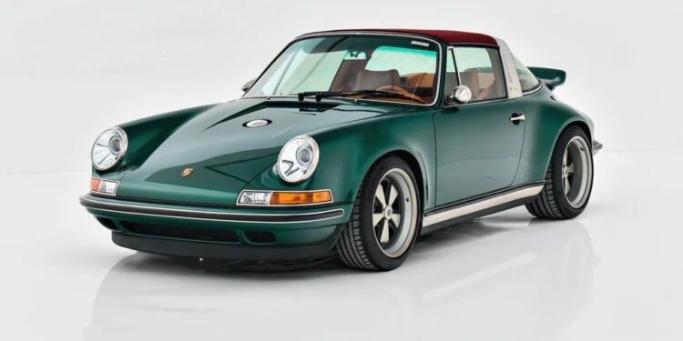 A classic dark green Porsche sports car with a red roof and tan interior is parked on a white reflective surface, viewed from the front left angle.
