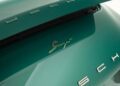 Close-up of a green Porsche with a gold "Singer" badge on the rear, partially showing the open engine cover and the "Porsche" lettering.