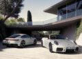 Two silver Porsche 911 sports cars, one coupe and one convertible, parked outside a modern house surrounded by greenery—a perfect showcase for Porsche’s 2025 reveals.