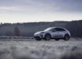 A white Porsche Macan Electric is parked on a frosty field with a forest in the background under an overcast sky, hinting at an adventurous road to Christ.