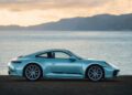 A silver Sonderwunsch 911 Carrera T is parked beside a body of water, with mountains rising in the background under a cloudy sky—a stunning Porsche scene reminiscent of Formosa’s scenic beauty.