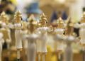 Close-up of several wooden figurines dressed in white robes and gold crowns, arranged in rows with a soft focus background—capturing the festive spirit on the road to Christmas.