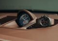A dashboard-mounted Porsche analog clock and a black chronograph wristwatch designed by F. A. Porsche rest on a brown leather 911 GT3 interior with air vents.