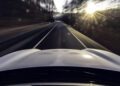 View from the hood of an Electric Porsche driving down a two-lane road, with sunlight streaming through trees and motion blur creating a dynamic scene—it's the perfect Road to Christmas.