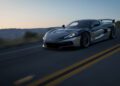 A sleek black Rimac Nevera R hypercar drives at high speed on an empty highway at sunset, with blurred surroundings indicating motion.
