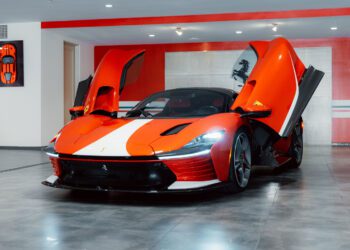 A Ferrari Daytona SP3, a true Modern Icon, with its scissor doors open is displayed in a modern showroom featuring gray tile floors and bold red and white wall accents.