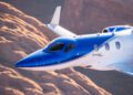 A blue and white HondaJet APMG airplane showcasing upgraded HondaJet performance as it soars over a rocky, desert landscape.