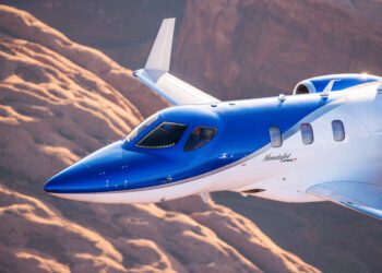 A blue and white HondaJet APMG airplane showcasing upgraded HondaJet performance as it soars over a rocky, desert landscape.