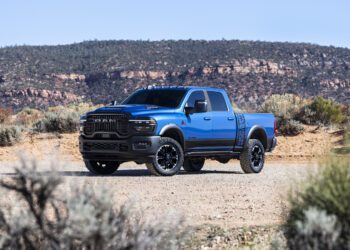 A blue 2027 Ram Power Wagon pickup truck is parked on a dirt road in a desert landscape with shrubs and rocky hills in the background, ready to showcase its impressive torque.